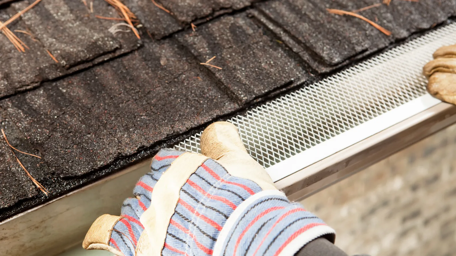 Mesh gutter guard being fitted by a roofer along a shingle roof edge
