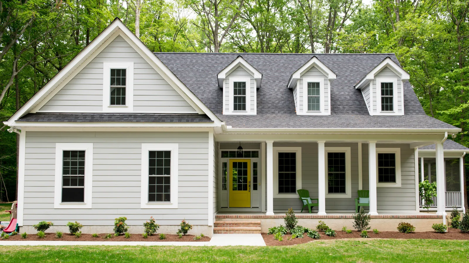 Yellow front door on a gray house with a dormered dark gray shingle roof