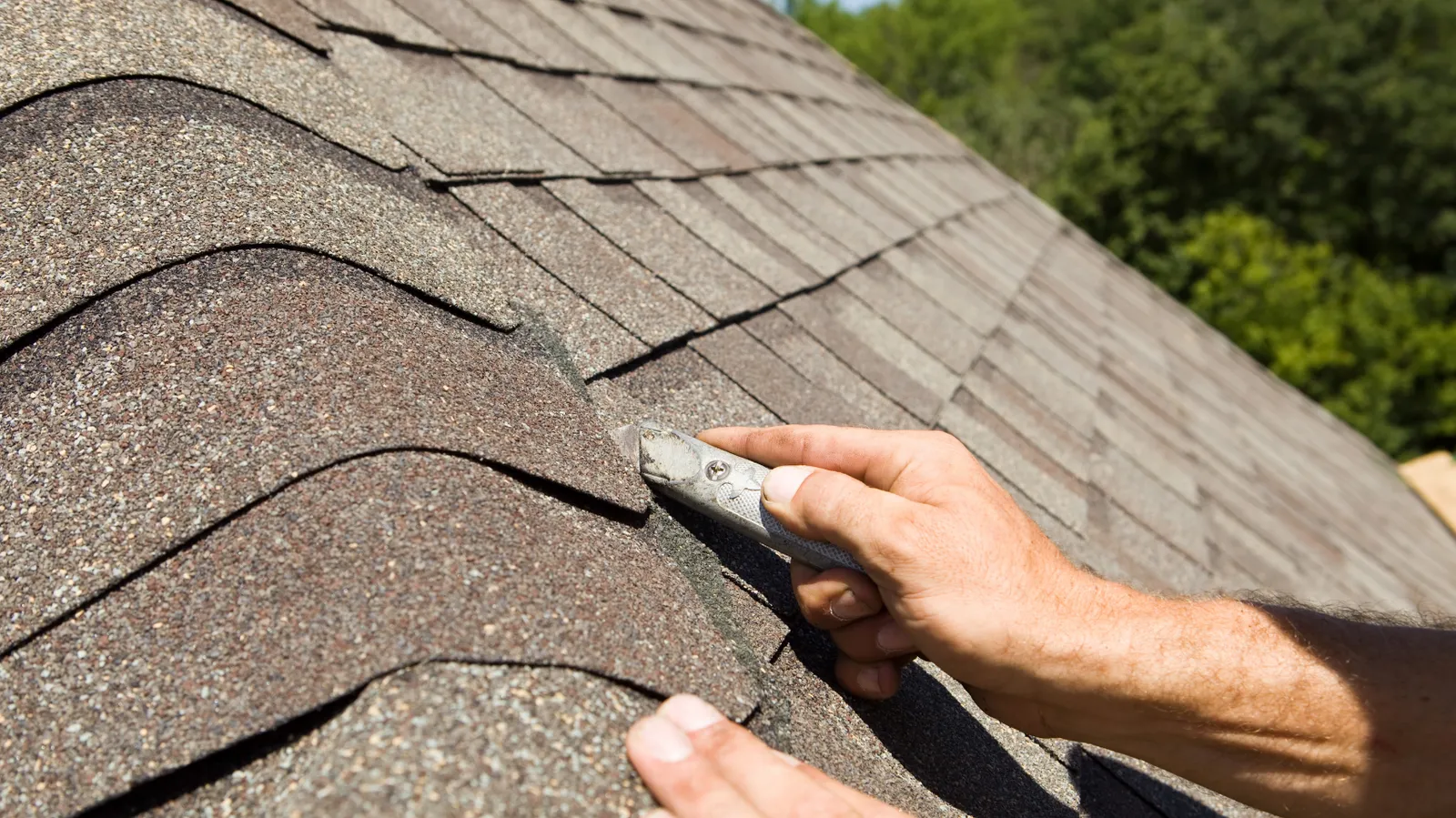 Utility knife in a roofer's hand trimming a ridge cap shingle