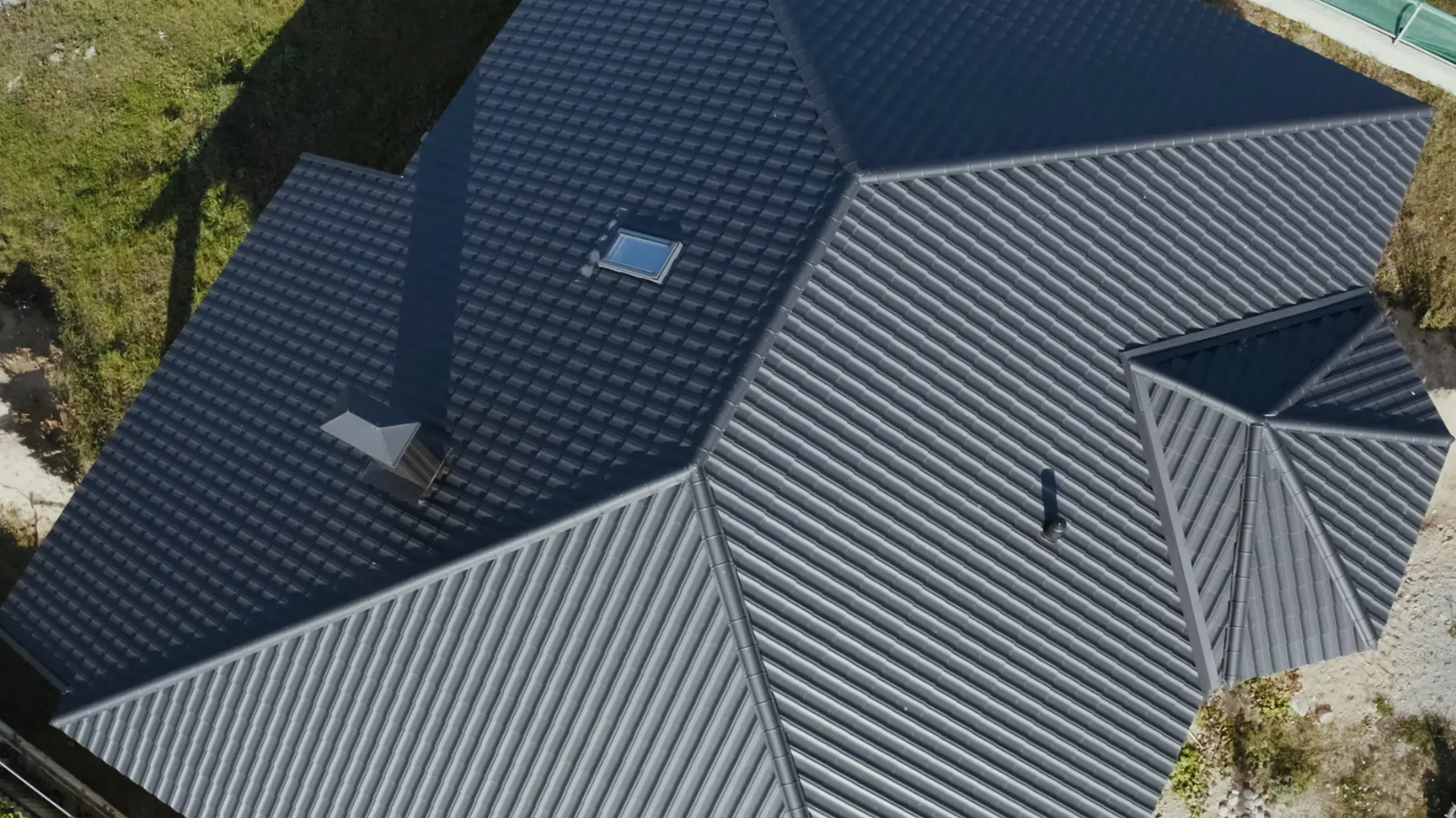 Brick gable and gutter beneath converging charcoal metal tile roof slopes
