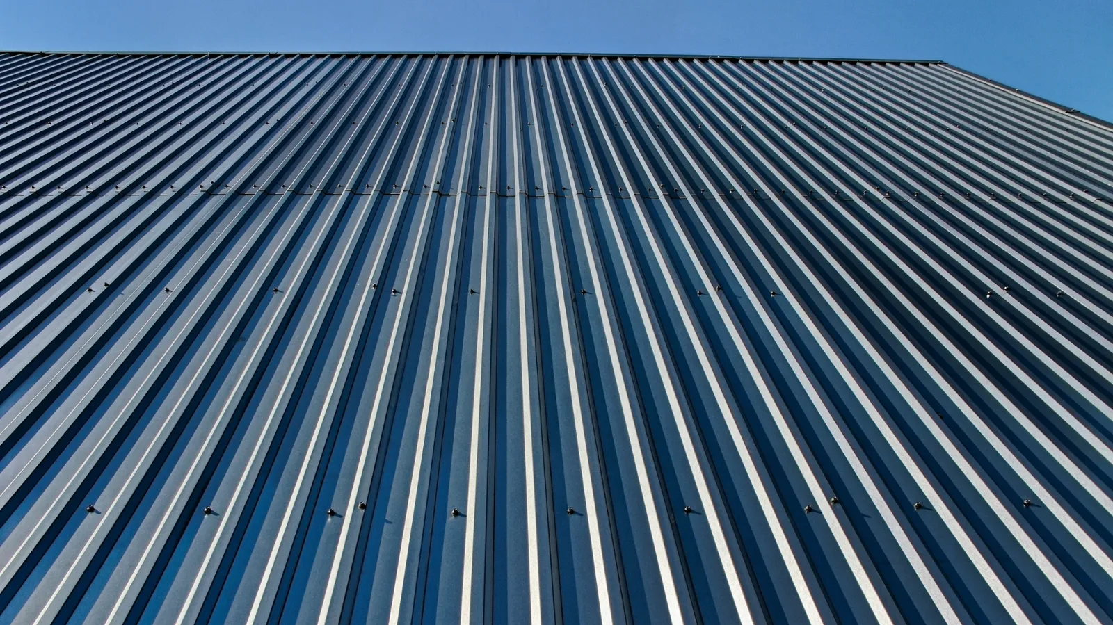 Ribbed metal cladding against a clear sky viewed from below