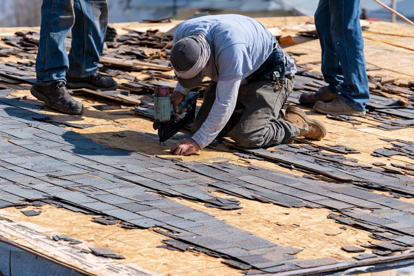 Partially stripped roof decking where a roofer kneels with a nail gun